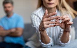 Woman removing her wedding ring while partner sits in the background, representing how divorce impacts health insurance in california.