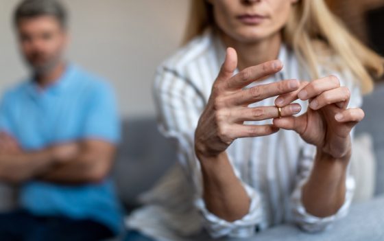 Woman removing her wedding ring while partner sits in the background, representing how divorce impacts health insurance in california.