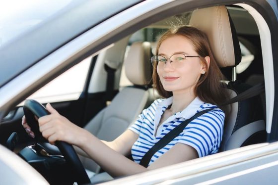 College-aged woman driving confidently with her seatbelt fastened, reflecting everyday independence supported by college student car insurance California.