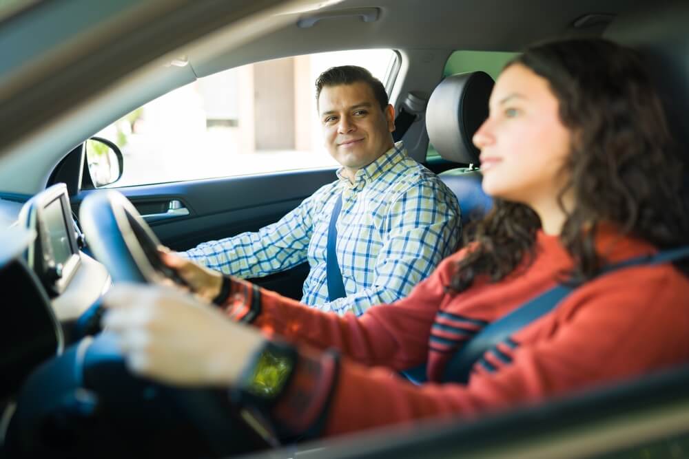 A father sits in the passenger seat while a college student drives, illustrating guidance and safety often associated with college student car insurance California.