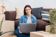 Student sitting among moving boxes with a laptop, representing the need for renters insurance for college students in California when moving into off-campus housing