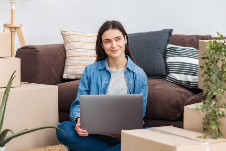 Student sitting among moving boxes with a laptop, representing the need for renters insurance for college students in California when moving into off-campus housing