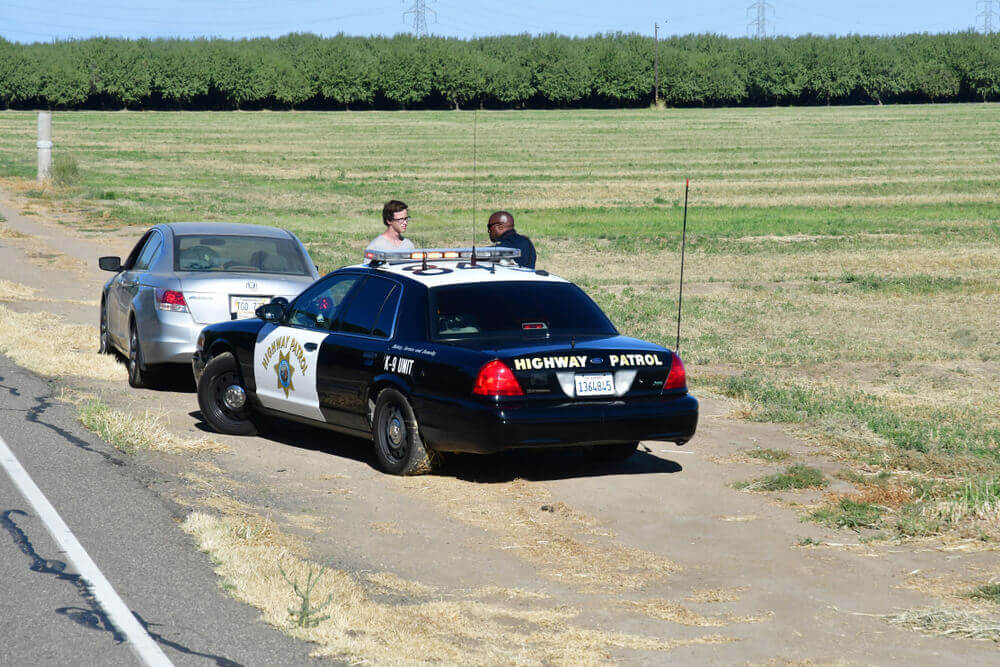 California highway patrol officer speaks with a driver during a roadside traffic stop on a rural highway, illustrating ticket vs. citation in California.