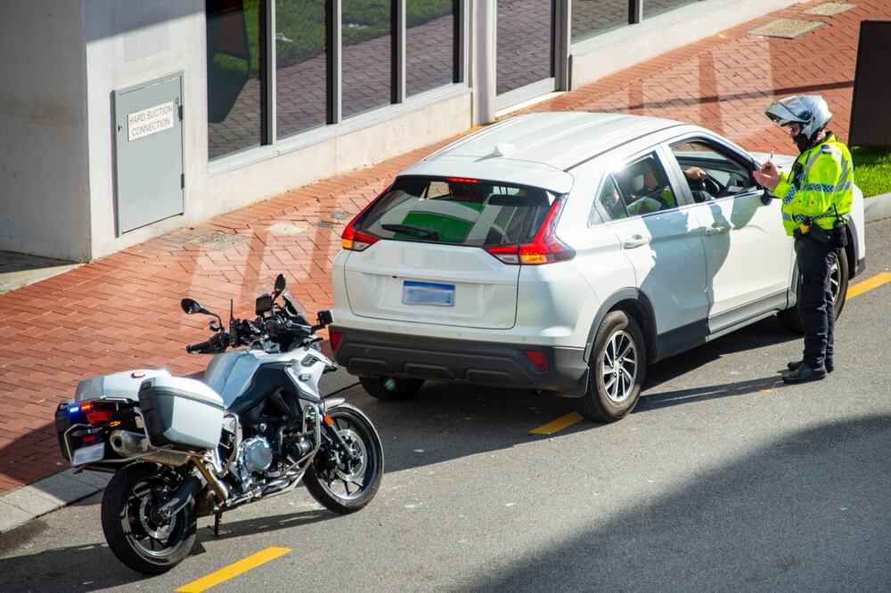 Police officer on a motorcycle stops a white suv and speaks with the driver on a city street, illustrating ticket vs. citation in california.