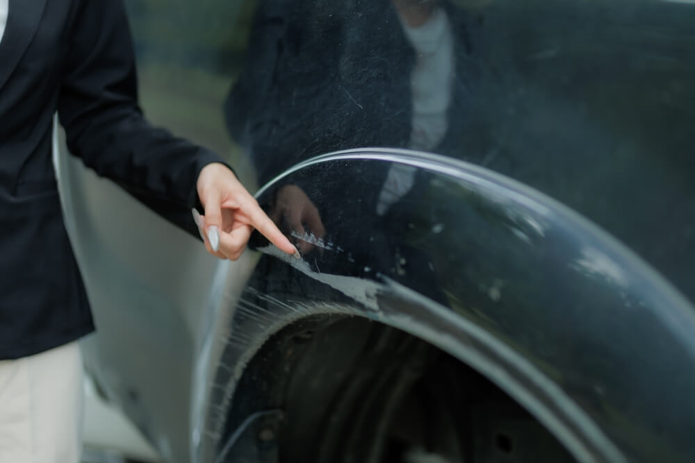 Person pointing at a scratch on a car door, illustrating a potential claim scenario involving car insurance out of state plates California.