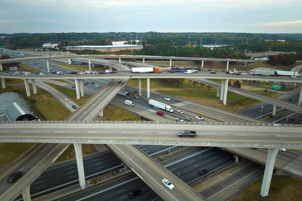 Aerial view of a multi-level freeway interchange with cars and semi-trucks moving across stacked overpasses, reflecting long-distance travel and car insurance for cross-state commuters in California.