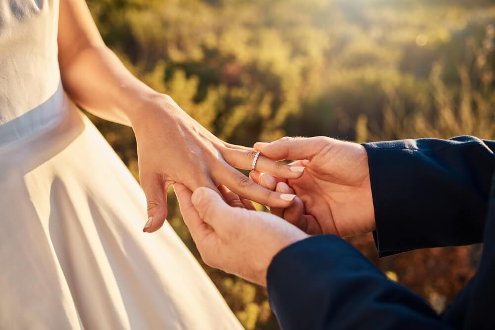 Couple exchanging wedding rings outdoors, illustrating a life event that may trigger a covered california income change update.