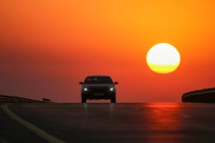 Car driving toward a bright sunset on an open highway, reminding drivers to update car insurance after moving california.