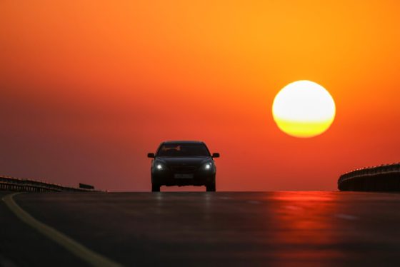 Car driving toward a bright sunset on an open highway, reminding drivers to update car insurance after moving california.