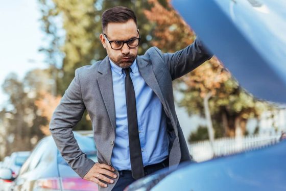 Businessman inspecting an open car hood after a breakdown, illustrating mechanical failures and car insurance coverage.