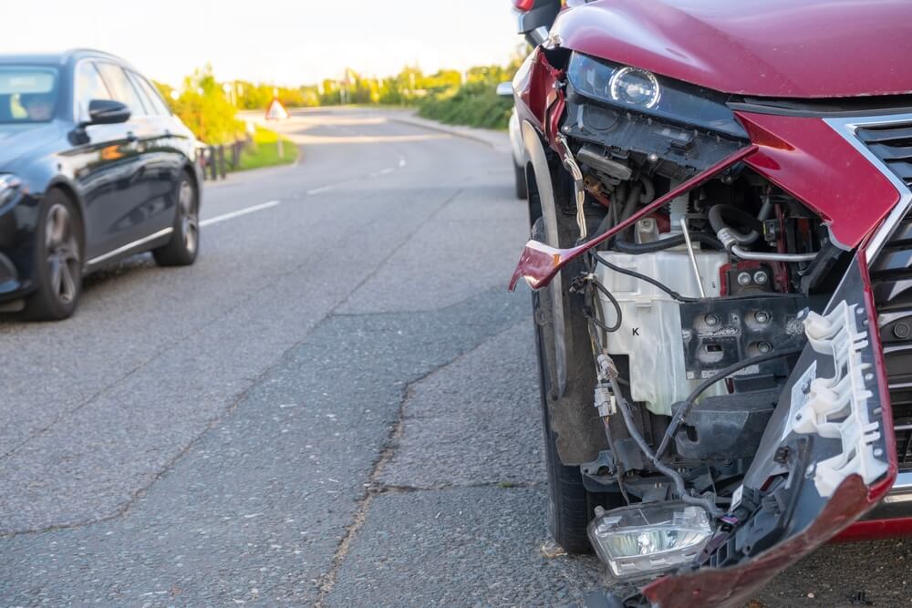Parked car hit and run in California shown through a red vehicle with front-end damage left on the side of the road.