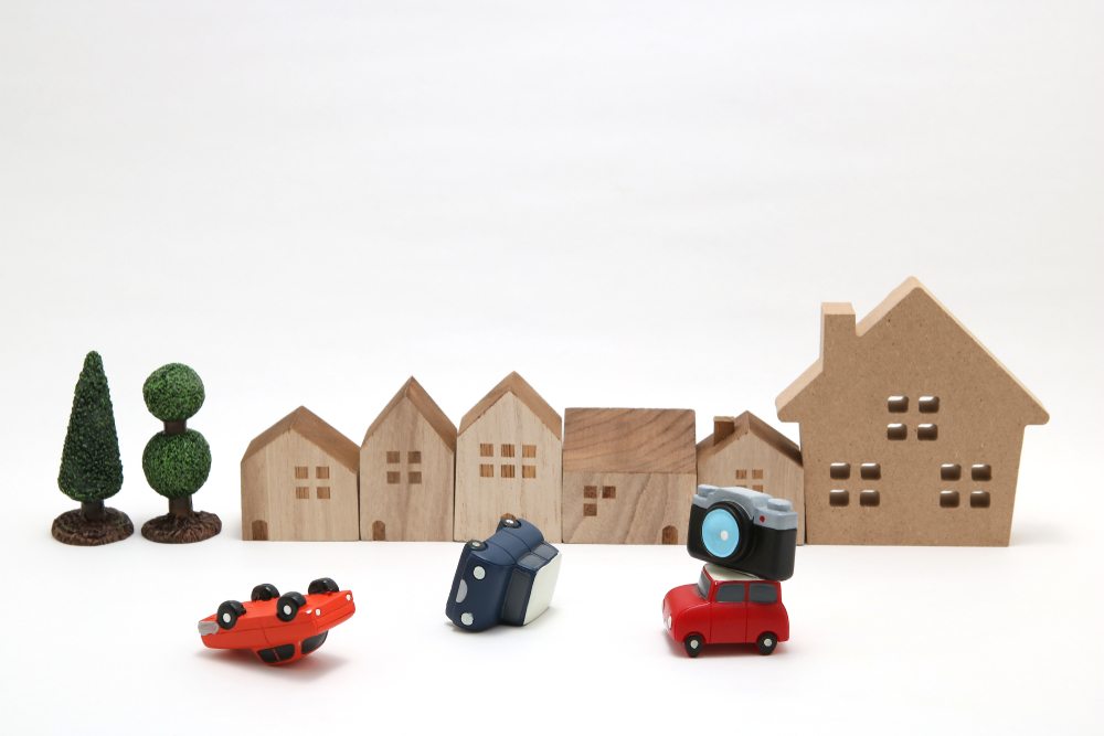 Toy cars and a camera sit in front of miniature houses, illustrating how dash cam footage can document car accidents for insurance claims.