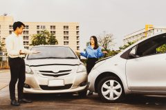 Two drivers stand beside two cars after a minor collision, illustrating a discussion about high versus low auto insurance deductibles.