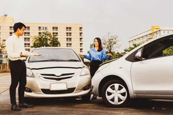 Two drivers stand beside two cars after a minor collision, illustrating a discussion about high versus low auto insurance deductibles.