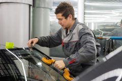 Auto glass technician replacing a car windshield in a repair shop.