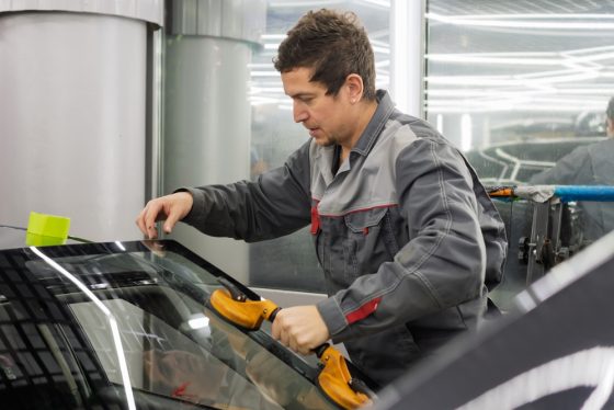 Auto glass technician replacing a car windshield in a repair shop.