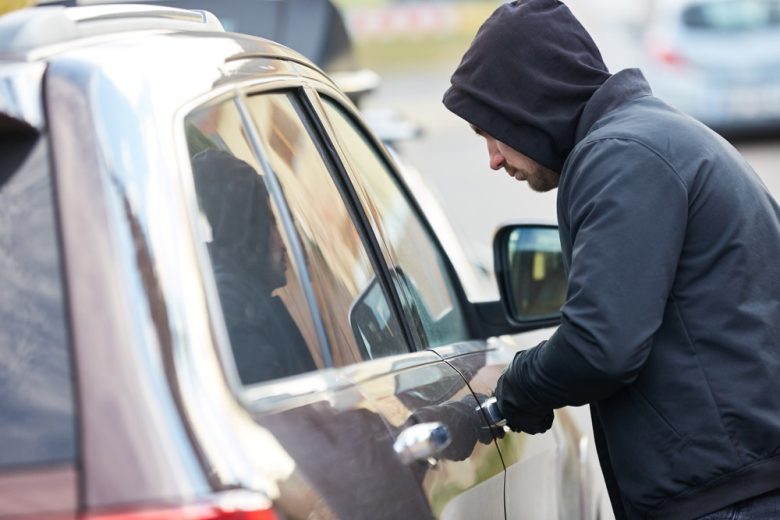 Man attempting to break into a vehicle, illustrating whether a comprehensive claim can raise car insurance rates in California.
