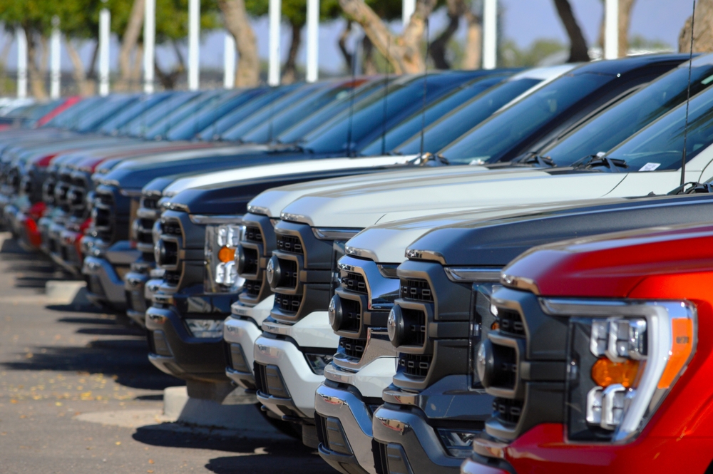 Rows of unsold new cars parked at a dealership.