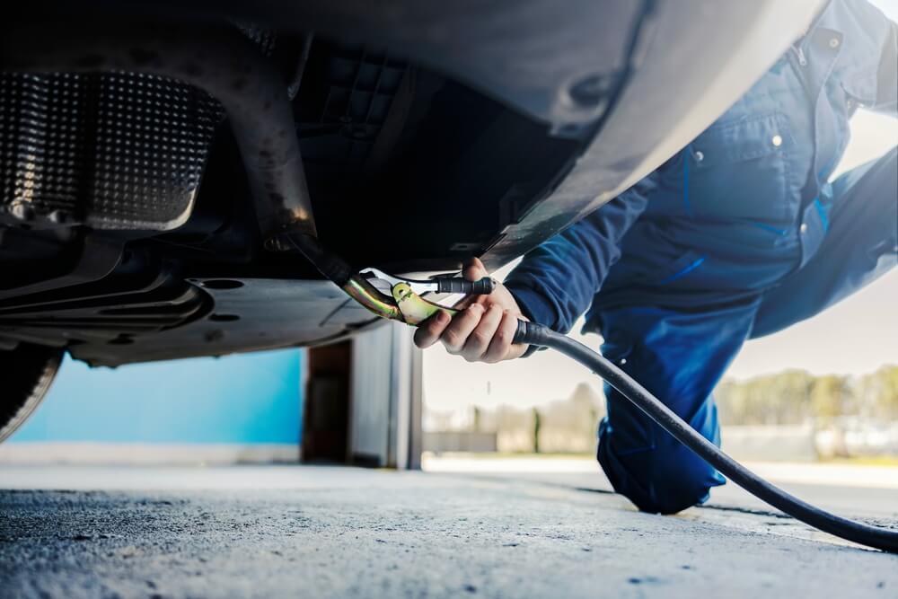 Técnico revisando la parte inferior de un auto durante una inspección, relacionada con el test de smog y la registración de mi vehículo.