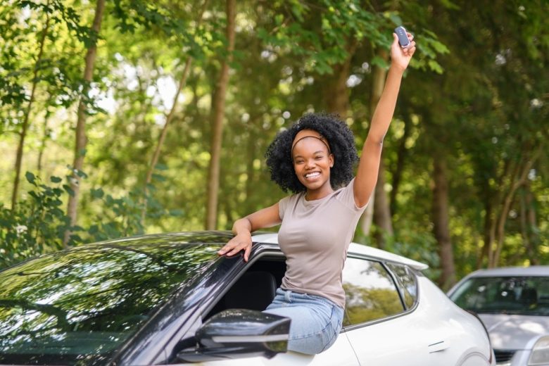 Mujer sonriente junto a su auto sosteniendo las llaves mientras conoce si el seguro GAP es reembolsable.