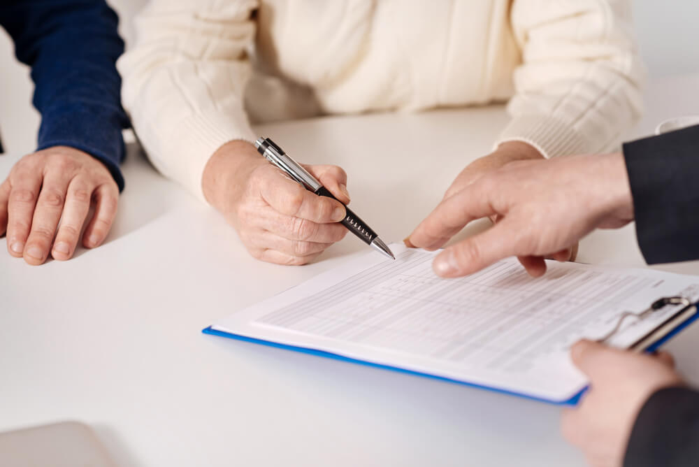 Persona firmando documentos con asesor, representando seguros de autos para hispanos en EE. UU.