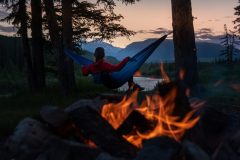 Persona descansando en una hamaca junto a una fogata en un campamento rodeado de naturaleza en California, cerca de San Diego y Los Ángeles.