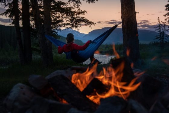 Persona descansando en una hamaca junto a una fogata en un campamento rodeado de naturaleza en California, cerca de San Diego y Los Ángeles.