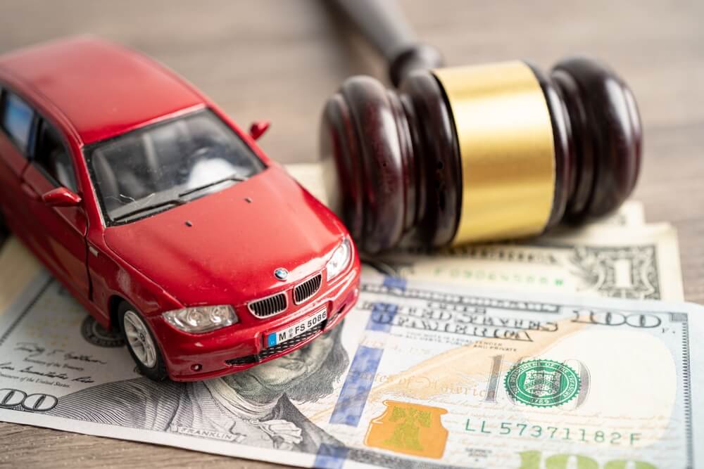 Martillo de subasta, dinero y automóvil en miniatura, representando los requisitos para comprar carros en subasta y los costos involucrados.