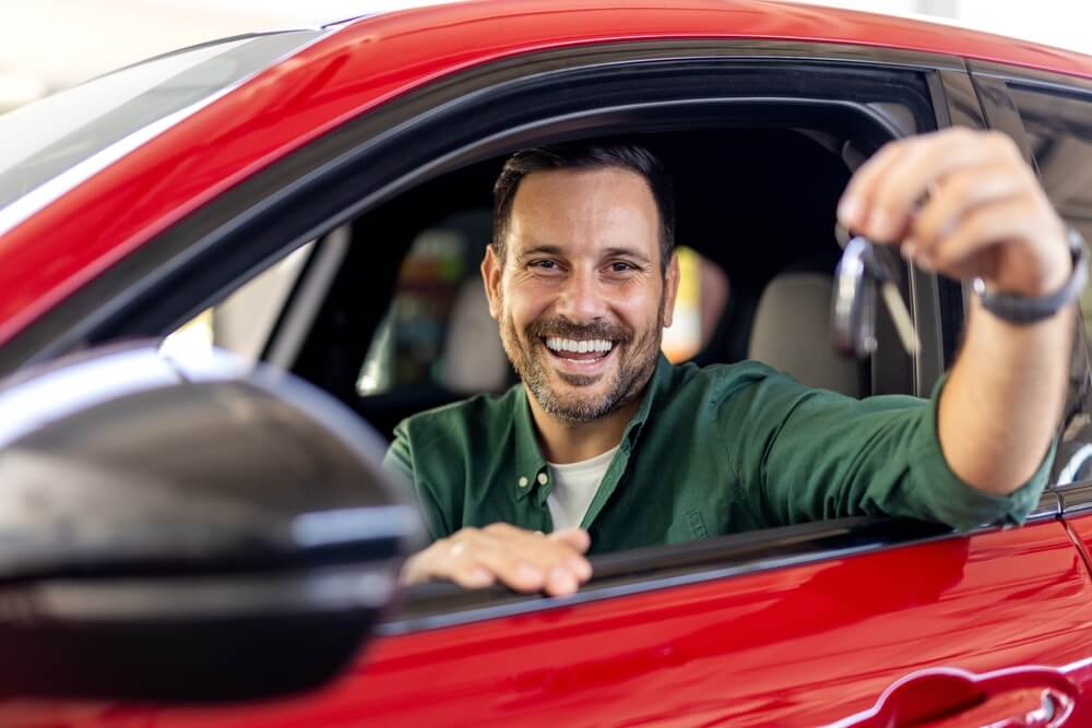 Comprador sonriente mostrando las llaves de un vehículo recién adquirido en una subasta de autos.