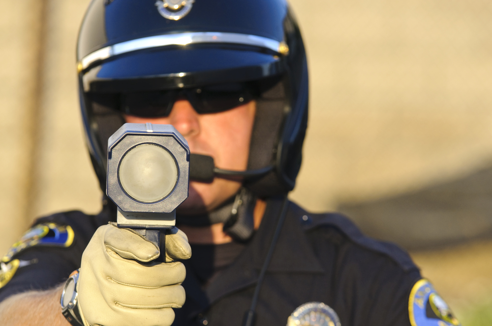 Agente de policía apuntando con su radar al tráfico que circula a gran velocidad. Multa por exceso de velocidad - Cost-U-Less