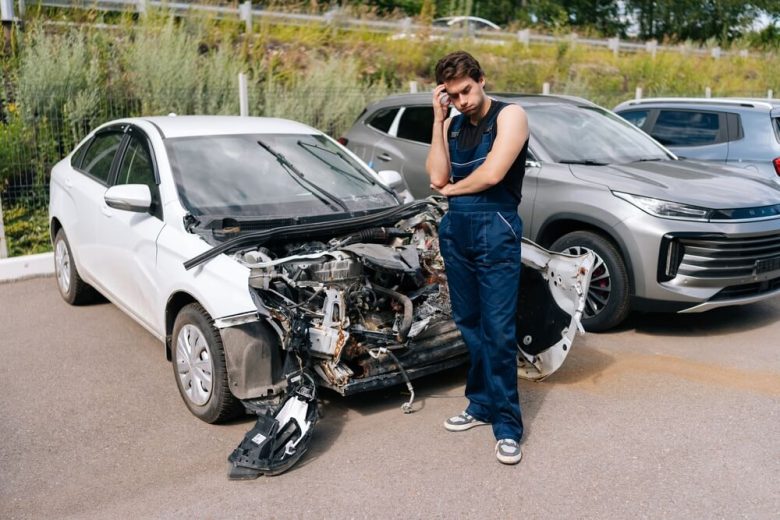 Mecánico observa con preocupación un auto blanco con daños severos en la parte frontal, una situación que puede relacionarse con un título salvage en USA.