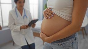 Mujer embarazada con el vientre visible en una sala de clínica mientras el médico ofrece una consulta médica gracias a su seguro de salud