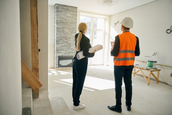 Profesional y contratista revisan planos en casa en obra, evaluando seguro de hogar durante remodelación en California