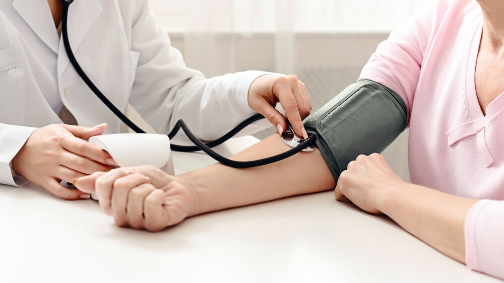 Profesional de la salud tomando la presión arterial a una paciente, representando los servicios preventivos que podrías dejar de aprovechar si no usas tu seguro de salud.