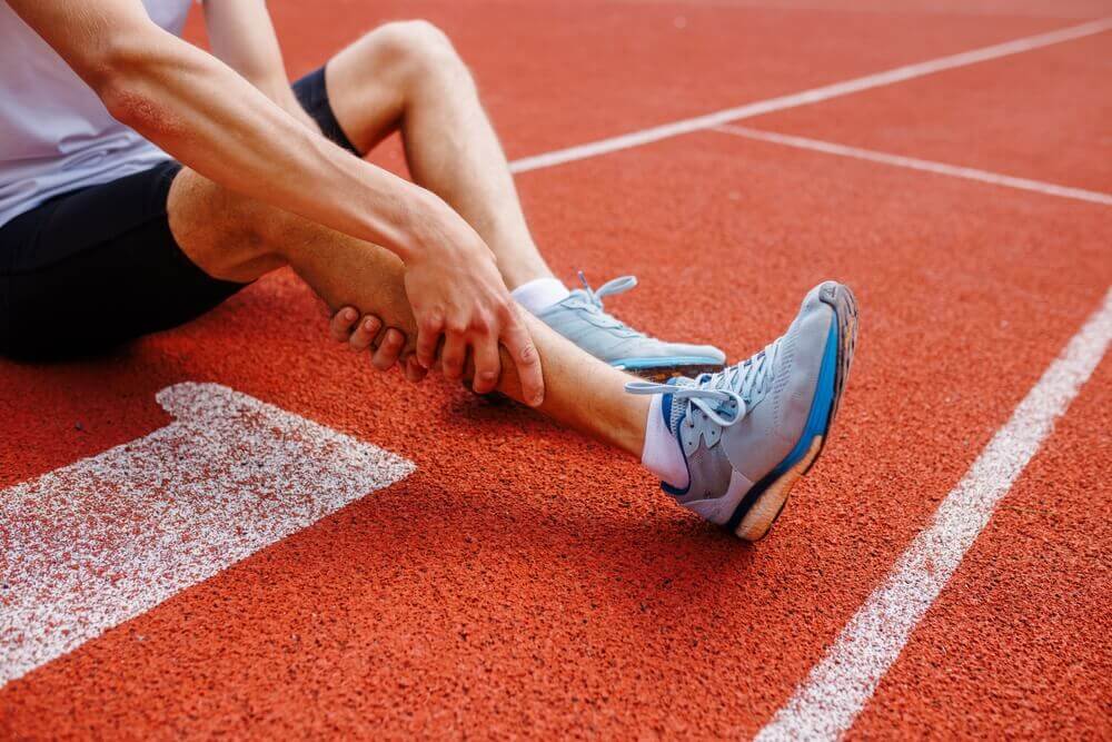 Corredor sujetándose el tobillo tras sufrir una lesión deportiva en una pista de atletismo.