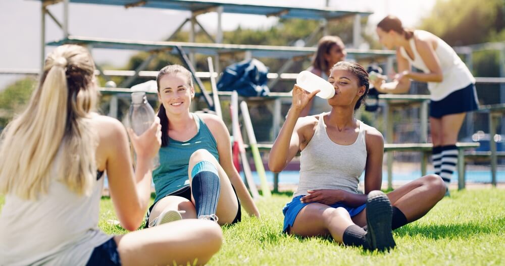 Grupo de deportistas descansando e hidratándose después de entrenar en una cancha deportiva al aire libre.