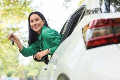 Conductora sonriente muestra las llaves desde la ventana de su auto, lista para revisar su seguro después de pagar por completo tu auto.
