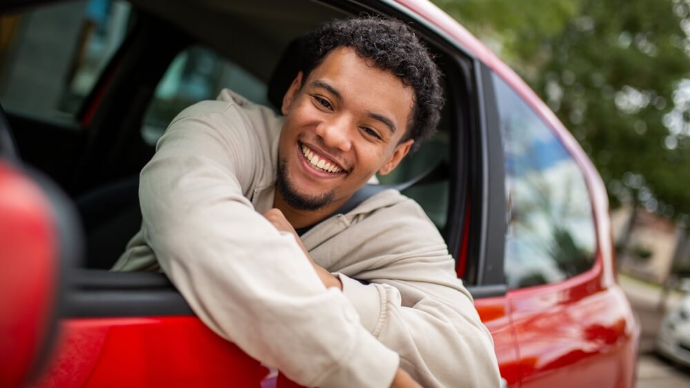 Conductor sonriente dentro de su auto pagado, disfrutando el momento mientras considera su seguro después de pagar por completo tu auto.