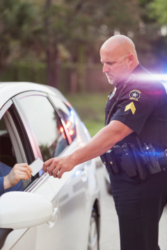 Policeman pulls over a driver for speeding.  Male driver is handing over his identification card.