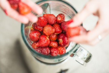 Fresh strawberries putting in blender cup and hands with some berries are blurry.