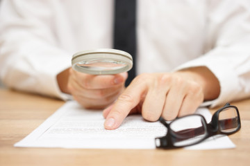 Focused businessman is reading through magnifying glass document