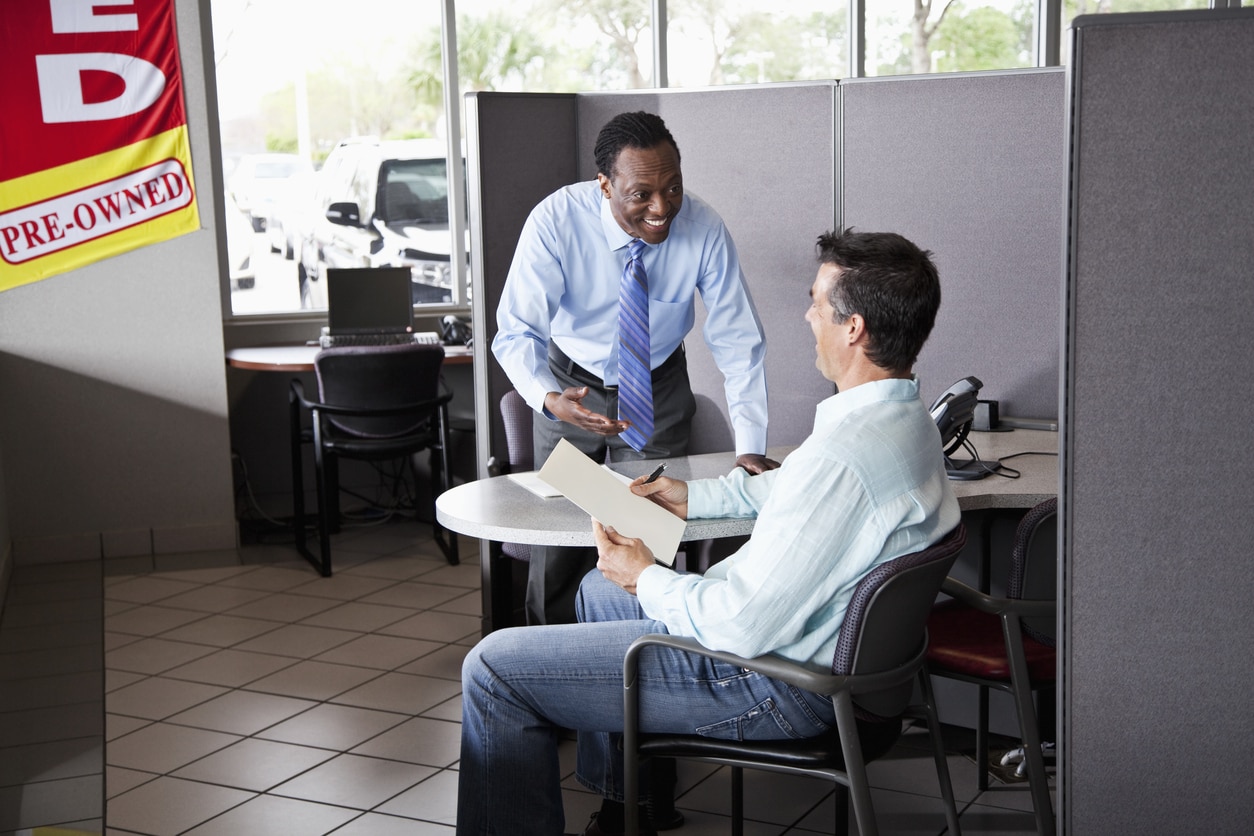 Car salesman with customer signing paperwork to buy used car