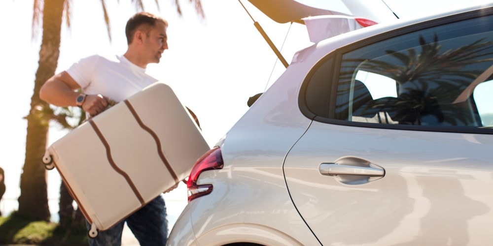 man putting suitcase in car trunk rental car insurance