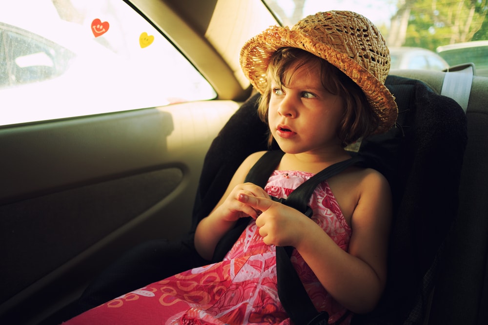 Little girl with a hat sitting inside a car on car seat