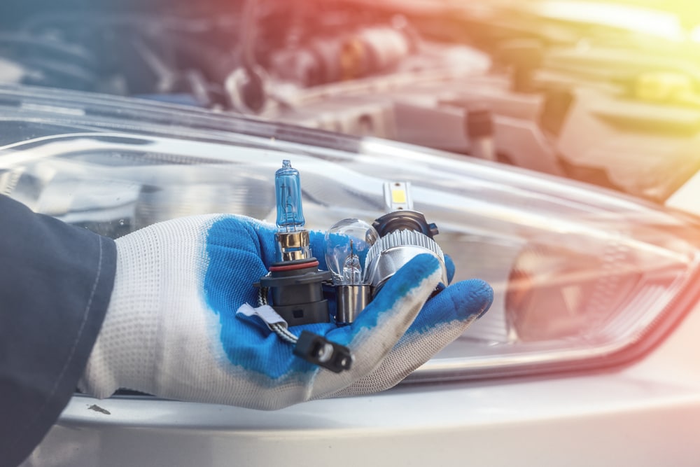 mechanic in front of car headlight holding led, hid and halogen bulbs