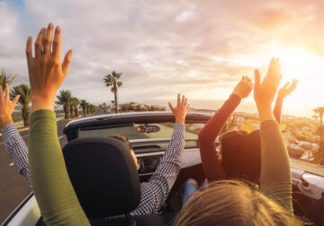 four young people raising hand in convertible car
