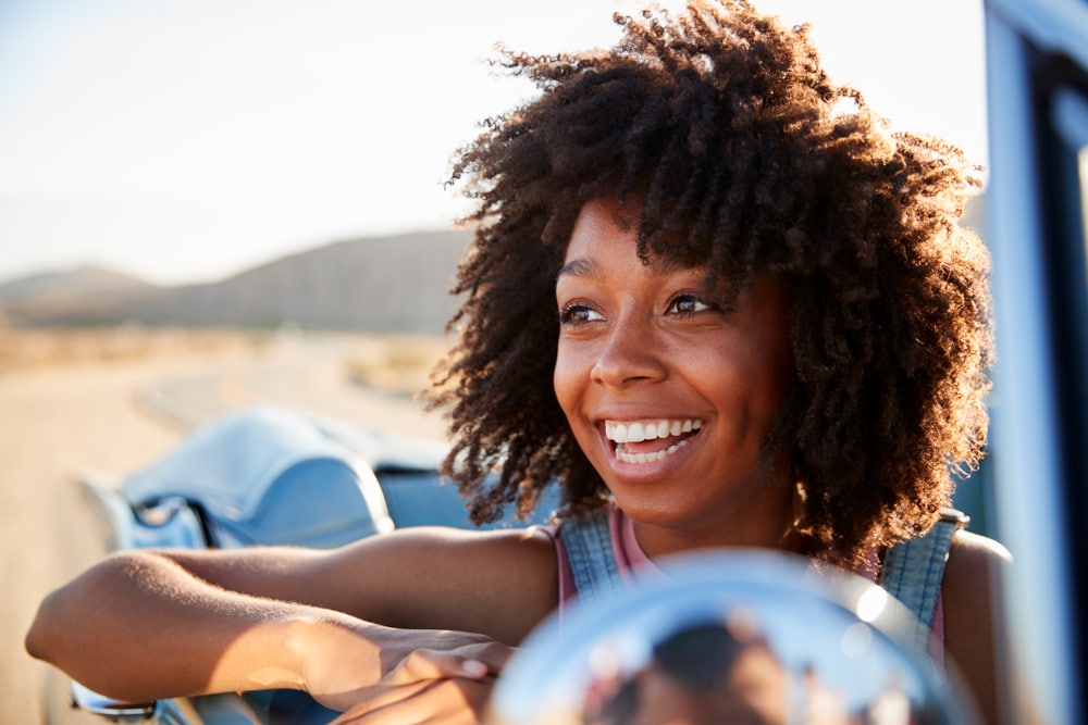 happy young woman on convertible car in a california road with cheap car insurance