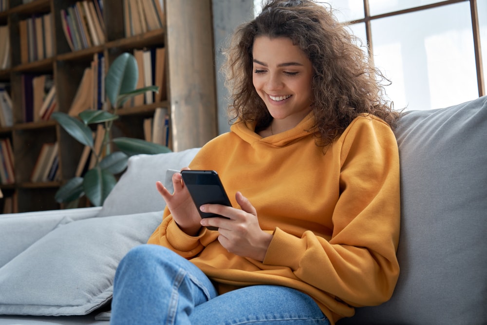 happy hispanic young woman looking at cheap car insurance in her phone