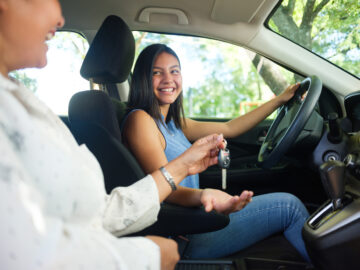 Teenage girl in a car as her mother sits next to her and hands her the keys to drive