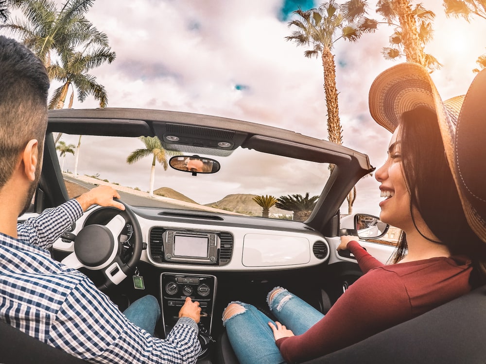 happy hispanic couple on car with cheap auto insurance